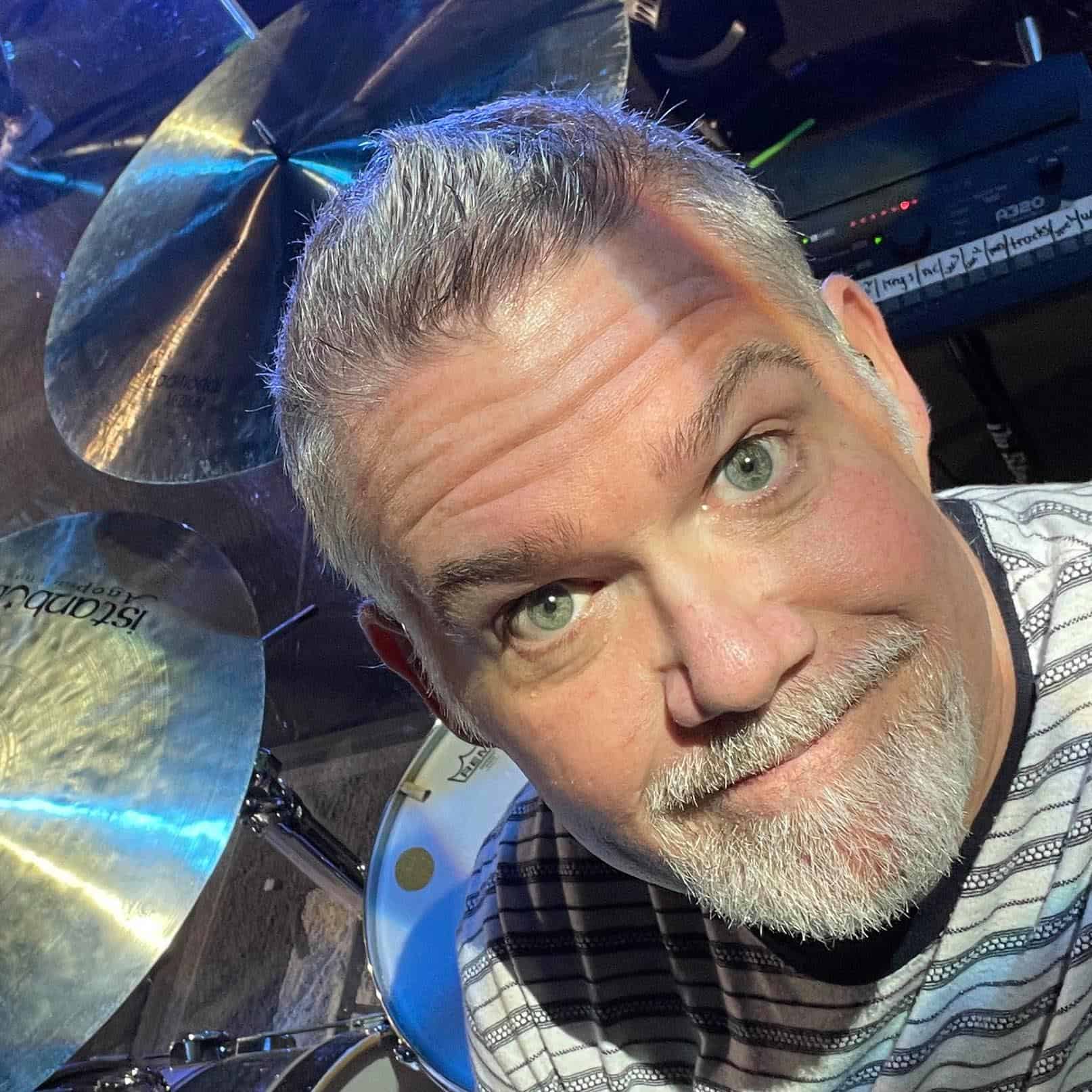 A man with a beard in front of a drum set.