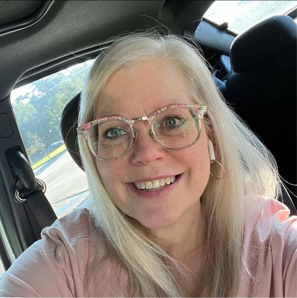 A woman in glasses sitting in the back seat of a car.